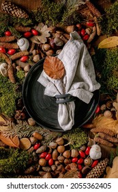 Empty black ceramic plate with cloth napkin over ambiance magic autumnal forest background. Autumn leaves, moss, fir cones, snail shell as surface. Autumn Thanksgiving menu. Flat lay