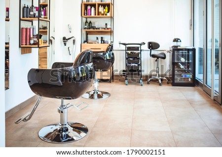 Empty black chairs and mirrors in barber shop. Interior of illuminated hair salon. Interior of modern hair salon. Empty interior of modern hairdressing salon