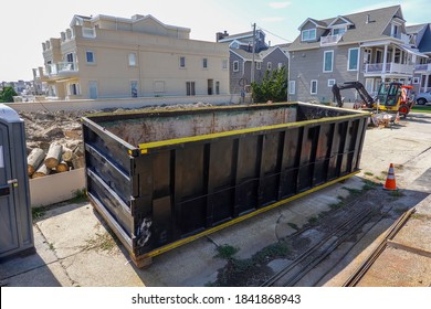 An Empty Black Dumpster Is Seen At A Construction Site Near A Backhoe