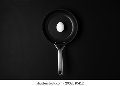 Empty Black Frying Pan On Black Wooden Table Background With White Raw Egg. Creative Food Art Cooking Concept.