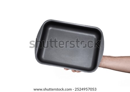 Empty, black, rectangular deep baking tray or casserole. Held by hand by Caucasian male hand. Close up studio shot, isolated on white.