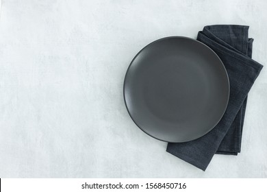 Empty Black Slate Plate On Grey Stone Table And Napkin. Food Background For Menu, Recipe. Table Setting. Flatlay, Top View. Mockup For Restaurant Dish