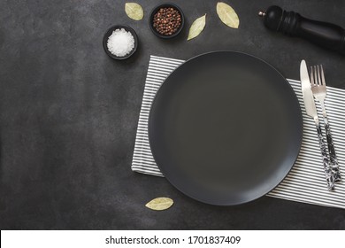 Empty Black Slate Plate On Black Stone Table And Napkin. Food Background For Menu, Recipe. Table Setting. Flatlay, Top View. Mockup For Restaurant Dish