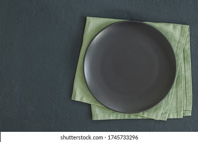 Empty Black Slate Plate On Dark Stone Table And Napkin. Food Background For Menu, Recipe. Table Setting. Flatlay, Top View. Mockup For Restaurant Dish
