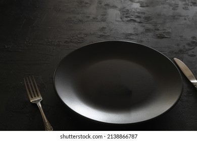 Empty Black Slate Plate On Dark Stone Table. Food Background For Menu, Recipe. Table Setting. Flatlay, Top View. Mockup For Restaurant Dish