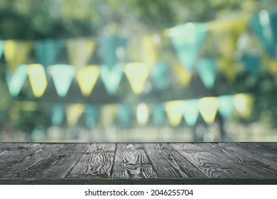 Empty Black Wooden Table In Park Decorated With Bunting Flags, Space For Design. Outdoor Party