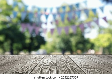 Empty Black Wooden Table In Park Decorated With Bunting Flags, Space For Design. Outdoor Party