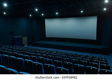 Empty blue cinema hall with white screen and seats. Side view
