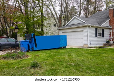 An empty blue dumpster in the driveway of a house