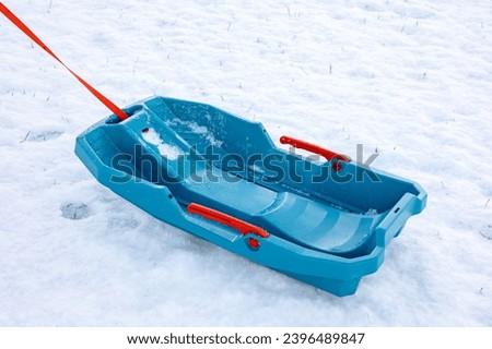 Empty blue plastic sled with a red rope lies on a snow-covered ground.space for text.
