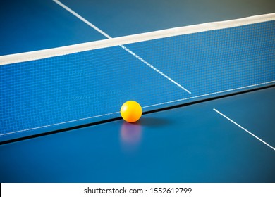 Empty blue table with a net and a yellow ball. Concept of table tennis and relaxing games during break for office workers. Place for text. Copyspace