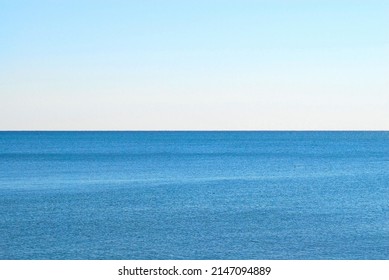 Empty Blue Water With Ripples Against Straight Horizon On Empty Pale Blue Sky.