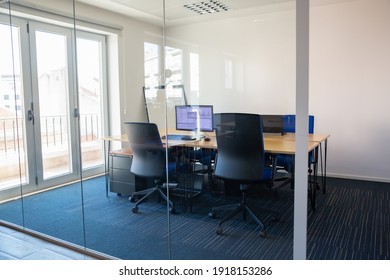 Empty Boardroom Behind Glass Wall. Meeting Room With Conference Table, Shared Desk For Team And Workplaces. Trading Graphs On Monitor. Office Interior Or Commercial Real Estate Concept