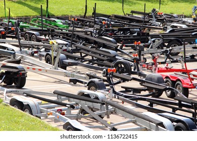 A Lot Of Empty Boat Trailers With Lodgements At The Yacht Club Parking In The Summer Against The Background Of Asphalt And Green Grass – Transportation And Storage Of Boats