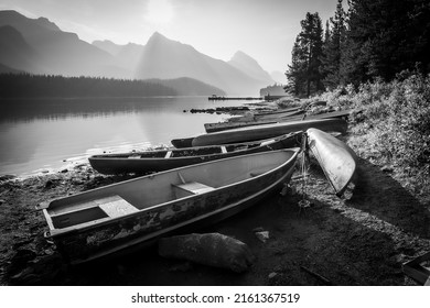 Empty boats lined up on the edge of a lake surrounded by mountains, monochromatic, Jasper NP, Canada