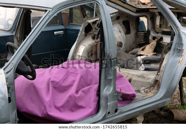 Empty body of an old\
disassembled car with a pink seating bag. Steering wheel, fabric\
bag in the interior of an old car. Body of the car without windows\
and doors.