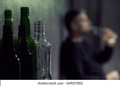 Empty Bottles Of Alcohol With Drinking Man