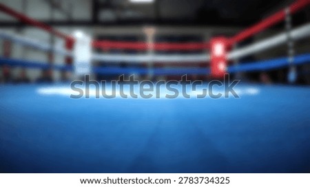 An empty boxing ring with a blue mat and red and white ropes is shown from a low angle inside a gymnasium.