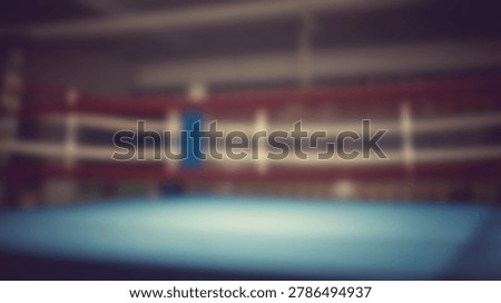 An empty boxing ring with a blue mat and red and white ropes is shown in a dimly lit arena with a vintage effect.