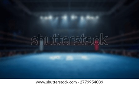 An empty boxing ring is illuminated by spotlights, creating a dramatic atmosphere. The blurred background adds depth to the scene.