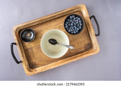 Empty Breakfast Bowl With Hints Of Healthy Oatmeal, Bowl Of Fresh Blueberries, On A Rustic Wood Serving Tray
