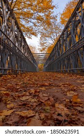 An empty bridge crosses the stream below Mountview Falls in Hamilton, covered with colourful fallen Autumn leaves on a bright sunny day.