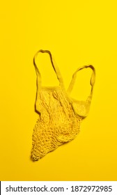 Empty Bright Yellow Mesh Bag On Yellow Paper Background. Flat Lay. Vertical Orientation. Conscious Consumerism And Eco Friendly Shopping Concept. Copy Space.