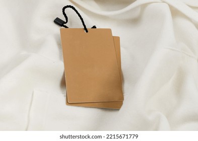 Empty Brown Cardboard Tag With String On White Jersey Hoodie. Vintage Paper Textured Mockup Cardboard Label. Price Tag, Gift Tag, Sale Tag, Address Label. Shopping Concept. 