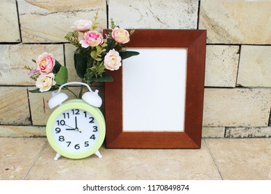 empty brown frame with alarm clock and artificial flowers. good for photos