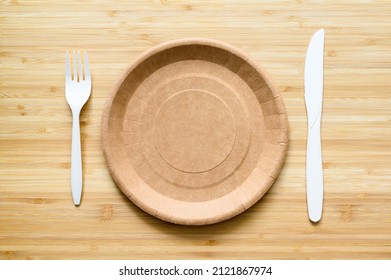 Empty Brown Paper Plate And Fork With Knife On A Wooden Table. View From Above. Eco-friendly Disposable Tableware. Copyspace.