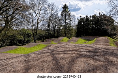 An empty, bumpy, dirt brown local BMX track verged with grass and plants in the Village of Nunney in a sunny day, Somerset, England, United Kingdom - 8th of April 2023