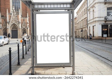 Empty Bus Stop Advertisement Frame in Krakow. High quality photoA blank advertising billboard stands at a modern bus stop on a cobbled street in Krakow. The empty frame is ready for a new ad, with old