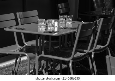 Empty Cafe Outdoor Terrace Setting For Lunch In Sunny Day. Nobody. Abandoned Lifestyle Background. Impossible Dinner Party, Socializing Limits, Economic Crisis Concepts. Black White Historic Photo