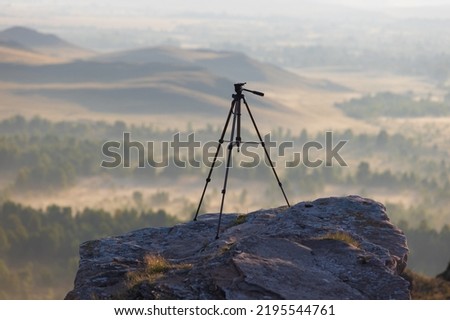 Empty camera tripod on top of a cliff against a blurred landscape