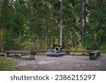 Empty campfire site with wooden benches and the concrete fire pit, side view. Hollola, Finland.