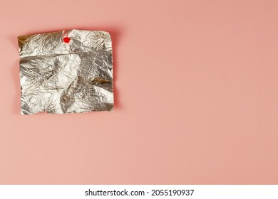 Empty Candy Wrapper Pinned To Pink Background. Rectangular Piece Of Crumpled Foil Vertically. Selective Focus.