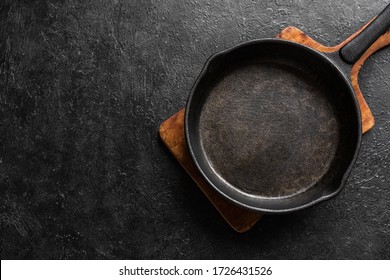 Empty cast iron frying pan for cooking on black background, top view, copy space. Cooking concept background with black pan.