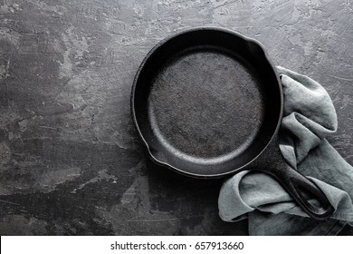 Empty cast iron frying pan on dark grey culinary background, view from above