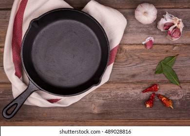 Empty Cast Iron Skillet With Herbs And Spices, Resting On A Tea Towel  Over An Old Wood Background. Retro Style Processing And Space For Your Text. 