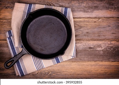 Empty Cast Iron Skillet With Tea Towel, Over Old Wood Background. Retro Style Processing And Space For Your Text. 