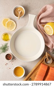 Empty ceramic baking dish surrounded by fresh ingredients for preparing honey mustard lemon salmon, including lemon, honey, mustard, herbs and seasonings. Healthy home cooking concept with high protein meal preparation, wholesome ingredients and rustic kitchen styling. Modern wellness nutrition, clean eating lifestyle and recipe background with copy space