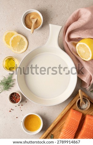 Empty ceramic baking dish surrounded by fresh ingredients for preparing honey mustard lemon salmon, including lemon, honey, mustard, herbs and seasonings. Healthy home cooking concept with high protein meal preparation, wholesome ingredients and rustic kitchen styling. Modern wellness nutrition, clean eating lifestyle and recipe background with copy space