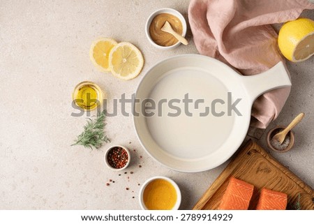 Empty ceramic baking dish surrounded by fresh ingredients for preparing honey mustard lemon salmon, including lemon, honey, mustard, herbs and seasonings. Healthy home cooking concept with high protein meal preparation, wholesome ingredients and rustic kitchen styling. Modern wellness nutrition, clean eating lifestyle and recipe background with copy space