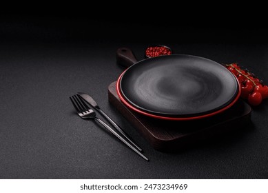 Empty ceramic round plate on dark textured concrete background. Cutlery, preparation for dinner