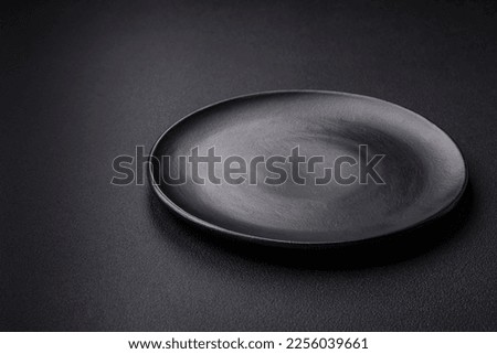 Empty ceramic round plate on dark textured concrete background. Cutlery, preparation for dinner