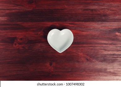 Empty ceramic saucer in the form of heart on a dark wooden table