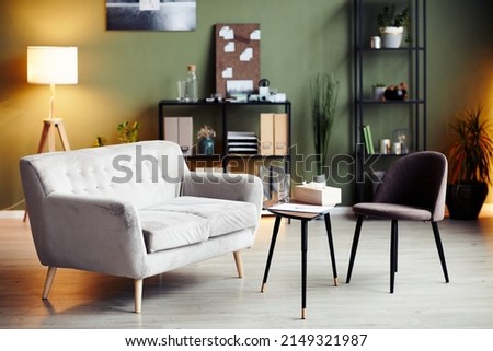Empty chair and sofa iin front of small table in office of psychologist