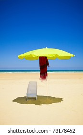 Empty chair and umbrella in a deserted sea beach with deep blue sky