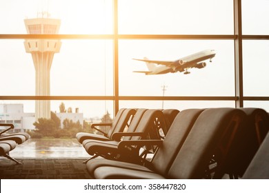 Empty chairs in the departure hall at airport , with the control tower and an airplane taking off at sunset. Travel and transportation concepts. - Shutterstock ID 358447820