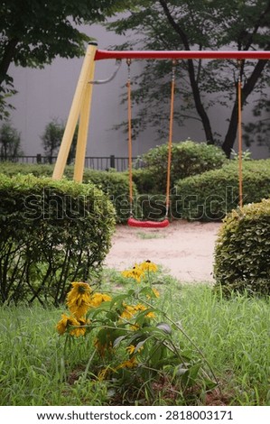 Empty children swing set in playground surrounded by bushes and yellow flowers, Korea